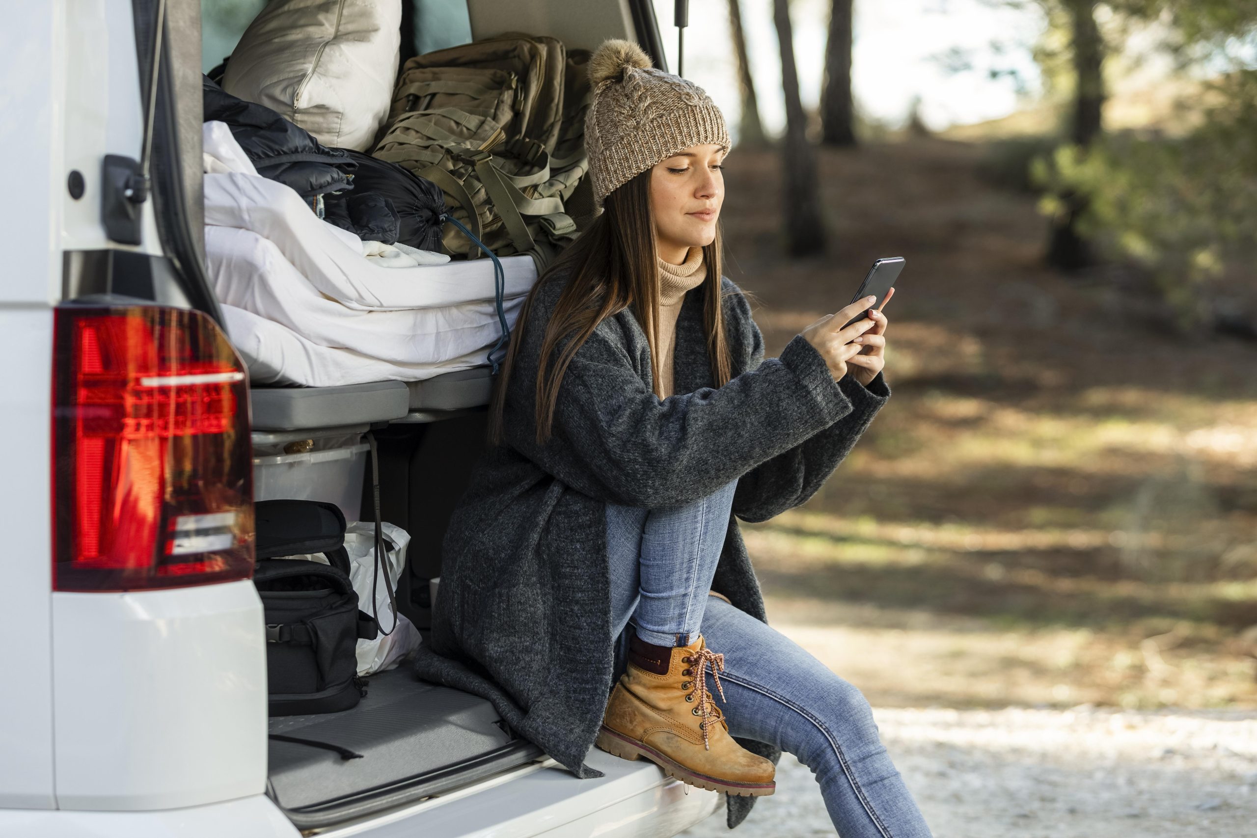 Vanlife au féminin : des pionnières aux voyageuses d’aujourd’hui 2 side view woman sitting trunk car while road trip using smartphone scaled